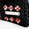 BOLSA MINI DE PERLA NEGRA CON LATERAL DERECHO BLANCA MANCHADA ROJO CON  6 FLORES AL FRENTE
